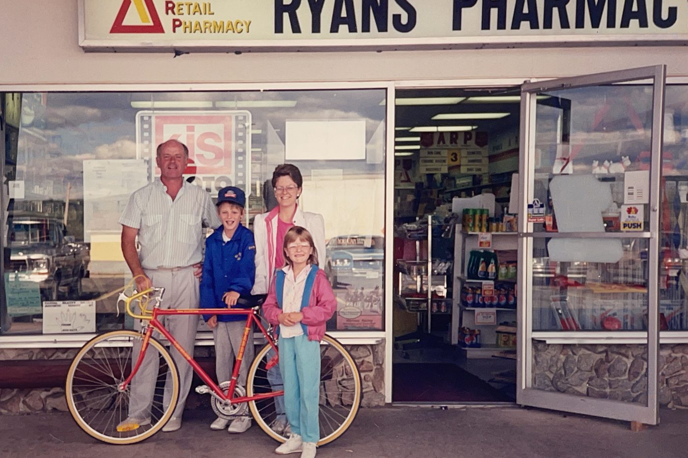 A young family posing with a bicycle outside the original Ryan's Pharmacy storefront in Nackawic